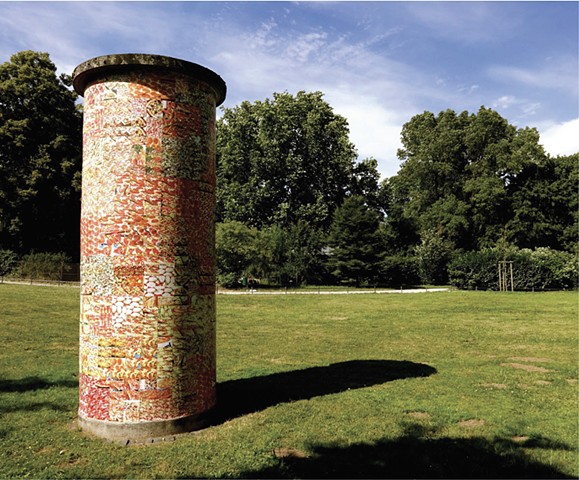 A Litfaßsäule in a park in the summer covered with photos of pizza