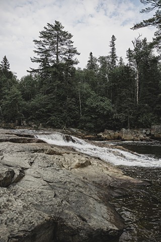 Water running over rocks with evergreen trees behind in Northern Ontario