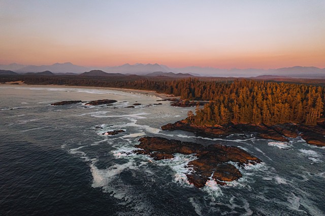 A drone shot of the ocean and beach in Torino, British Columbia at sunset with mountains in the background