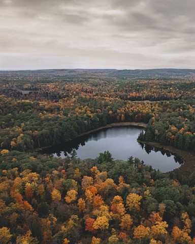 A drone shot of trees with fall foliage surrounding a heart-shaped lake in North Frontenac, Ontario