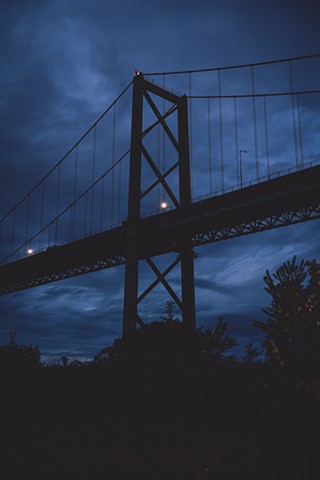 Silhouette of a bridge against a dark blue sky in Downtown Halifax with the ocean flowing under it
