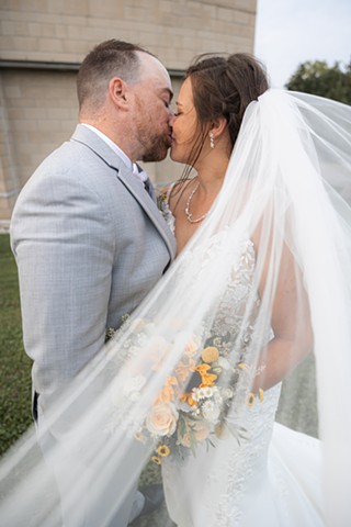 Bride and groom kissing with brides veil flowing in the wind toward the camera