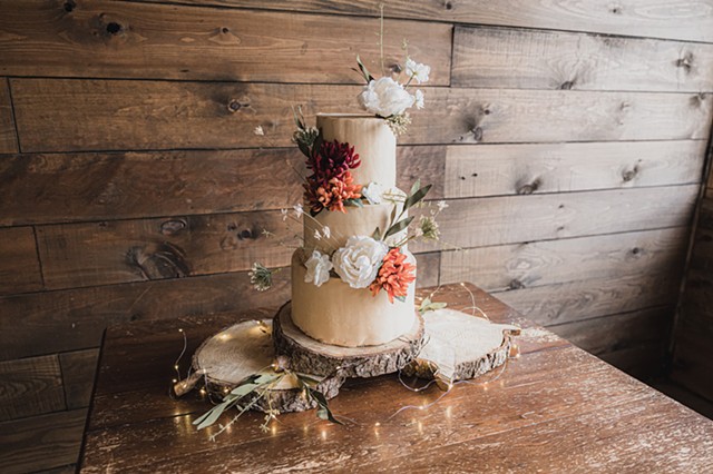 A wedding cake on a table covered with flowers and surrounded by twinkly lights
