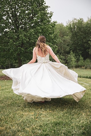 A bride spinning in a field in front of a tree with her dress flowing out all around her