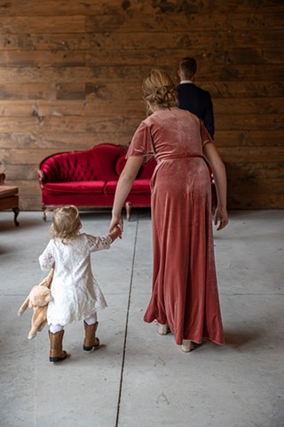 Grooms daughter in a pink dress, leading a toddler in a white dress towards their dad standing with his back to them