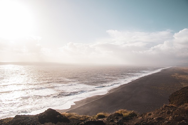A cliff overlooking the sun on the ocean with waves on a black sand beach in Iceland