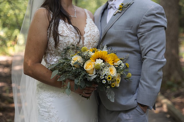 Bride and groom standing together while bride holds wedding bouquet with sunflowers