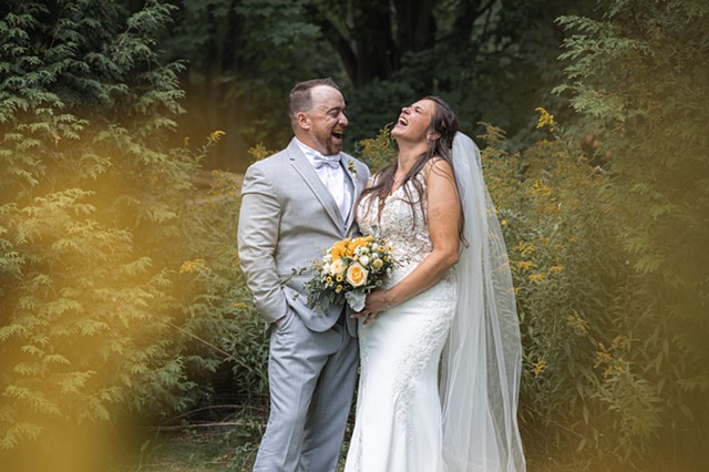 Bride and groom laughing together in an evergreen forest with yellow flowers all around