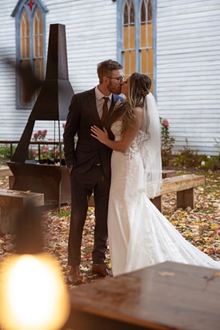 A bride and groom kissing in front of a church with fall leaves all around