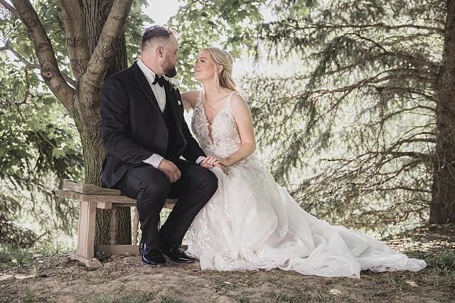 Bride and groom sitting in a bench in the forest together looking into each others eyes