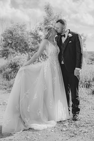 Black and white photo of bride and groom kissing with trees in the background
