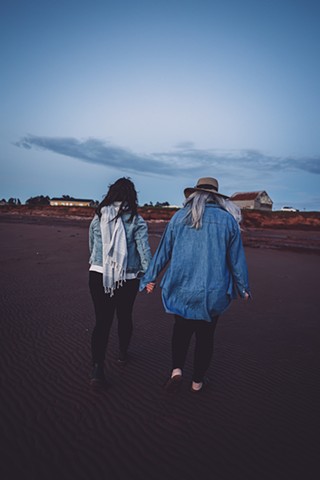 Two women walking hand in hand as the sun goes down on a red sand beach in Price Edward Island