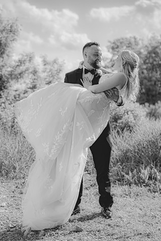 Groom carrying bride and smiling down at her while she smiles up at him