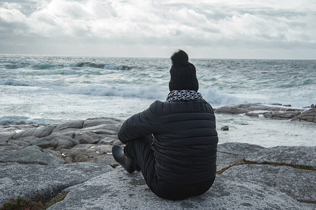 A woman sitting on rocks next to the sea watching ocean waves rolling in at Peggy's Cove