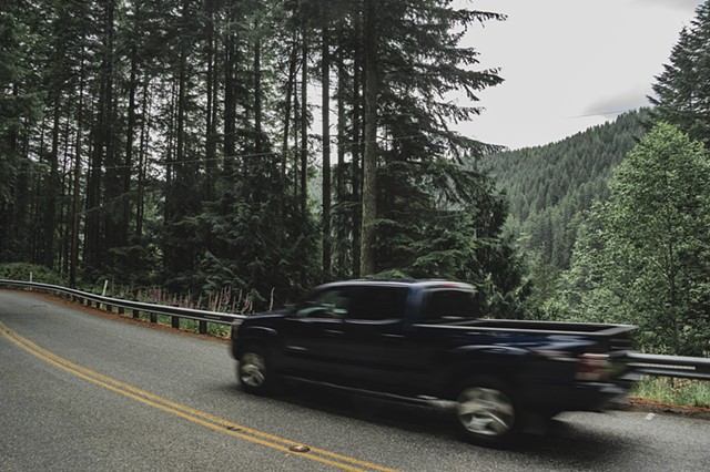 A blurry pick-up truck driving by on a highway in Mount Rainier National Park with evergreens in the background