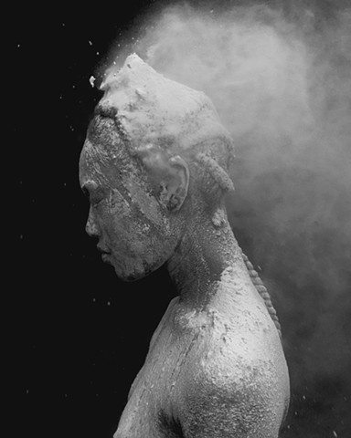 this is a photograph by los angeles based contemporary artist that is black and white of a figure that is covered in flour (not flowers). Esteban Schimpf made this artwork in California using a digital camera made by Fuji called the X100T. soon it will be