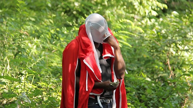 photograph of Black man in woods with red hoodie, stocking cap and money by Antoine Williams 
