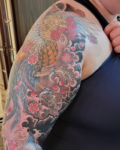 A tattoo on the arm of a nonbinary person, of a Japanese inspired fighting rooster, done in bold colour done by Jason Dopko at Good Times Tattoos in Saskatoon,Saskatchewan,Canada 