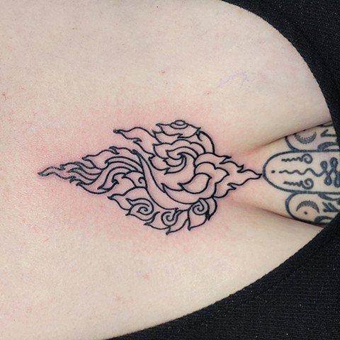 A woman's sternum tattooed with a bold outline of a flame design, inspired by Thai art done by Jason Dopko at Good Times Tattoos in Saskatoon