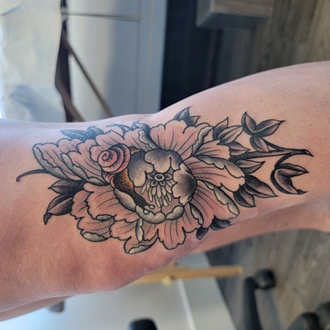 Peony and snail, tattooed in colour. The photo is of a woman in a Saskatoon tattoo shop. The snail is in colour and the flower is black and grey with accents.