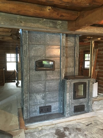 The kitchen side of this masonry heater features a white oven and a cooktop with it's own firebox.