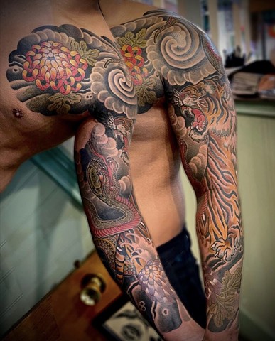 A traditional Japanese full sleeve, chest to wrist, featuring a tiger and snake, complimented by chrysanthemum flowers