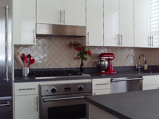 Open kitchen with island, warm neutral back splash, light cabinets,dark counter top and red accessories by Jane Interiors NYC.