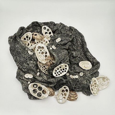 A sculpture of a sweater, dipped porcelain slip and burned away, with porcelain sculptures of mussel shells, some drilled as button blanks. 