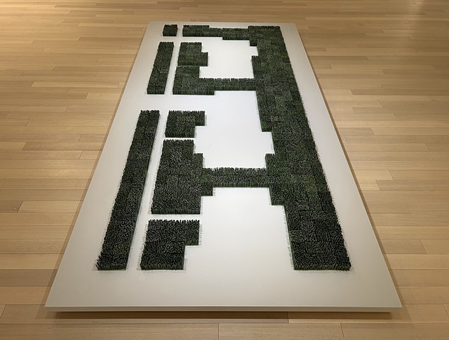 Am installation of porcelain grass in shape of a lawn with space for houses and driveways on white pedestal on a wooden floor
