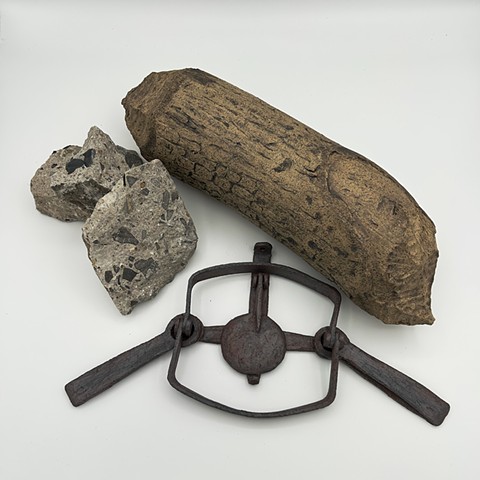 A still life sculpture with a chunk of found concrete, an antique-looking beaver trap made of iron red stoneware, and a beaver-chewed log made og speckled tan stoneware. 