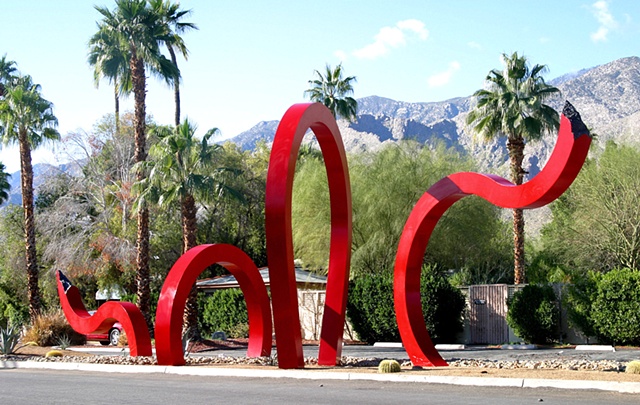 A monumental outdoor sculpture, "Jungle Red" is composed of large red fabricated steel beams that appears to move in and out of the ground in both a dramatic and whimsical style. 