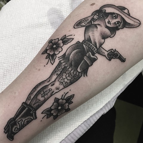 Traditional black and grey cowgirl pinup girl tattoo with guns cowboy boots hat and flowers. Made in Toronto