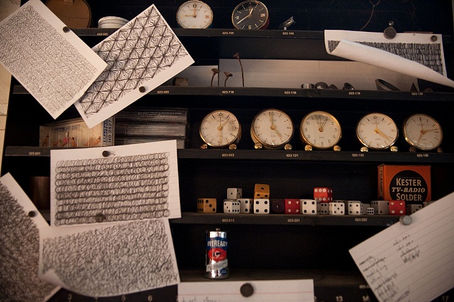 "Clocks, dice, and batteries and various machined objects sit on a shelf, surrounded by a handful of his precise, manic doodles."

