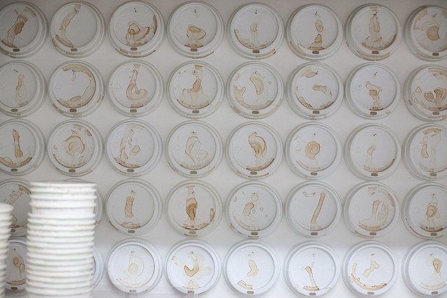 "A grid of coffee cup lids neatly arrayed on the studio wall creates an oddly organized counterpoint to the random spillage".