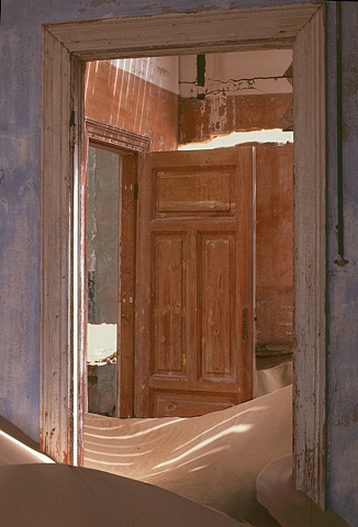 Kolmanskop Namibia, a deserted diamond mining town, blue walls with sand dunes in the room and shadow patterns on the sand