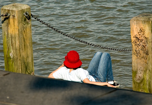 Person sitting on the steps of the River in New Orleans in a red hat watching the world go by