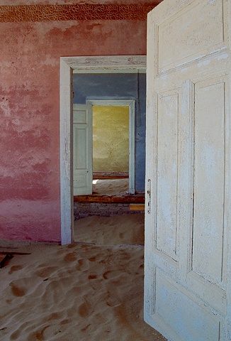 Kolmanskop Namibia, a deserted diamond mining town in the desert, doors aligned to see from the pink room, to the blue room to the yellow room, sand dunes in the house