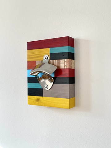 Wall mounted bottle opener from salvaged wood with translucent colors and polished stainless steel hardware.
