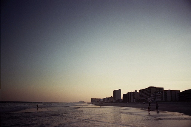 east coast low light buildings on right high angle on water child in water on left.