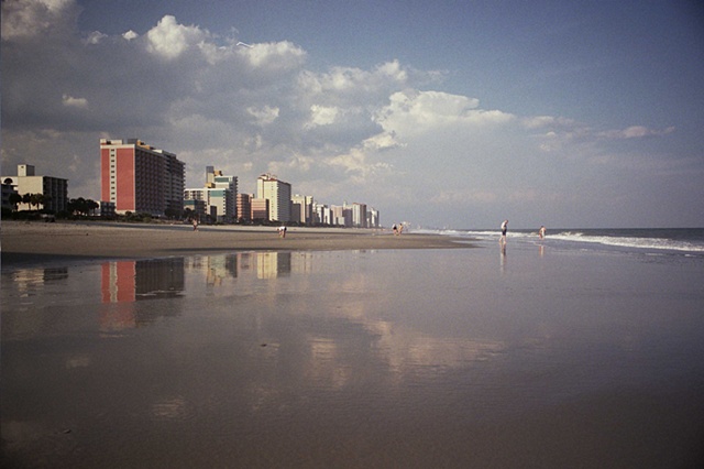east coast with buildings on left and reflective water in foreground. 
