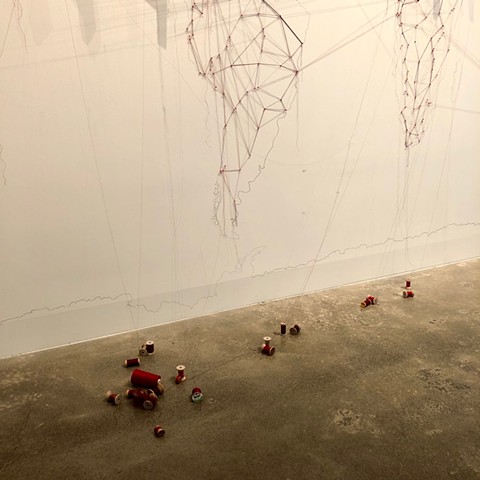 Detail of an installation about migrations completed at the San Francisco Arts Commission Gallery.  A large map of the world was drawn on the wall in graphite, map pins and red thread trace the paths of current major migrations. 