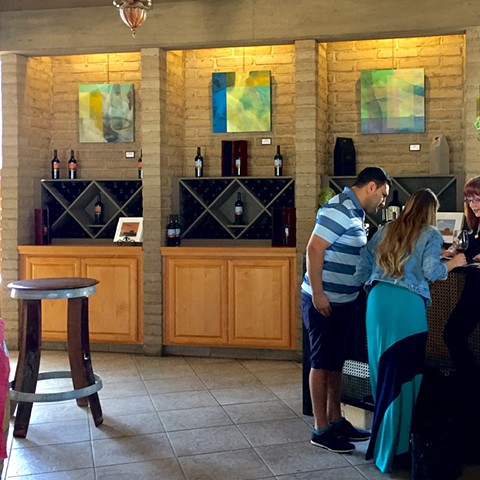 Three paintings on Wente walls with people in foreground wine tasting.