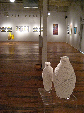 Different long angle view of the gallery space with vessels and paintings.