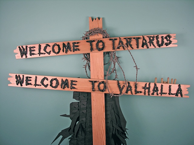 “Welcome to Tarturus, Welcome to Valhalla”; wooden stakes, tire, barbed wire, and bullets.
