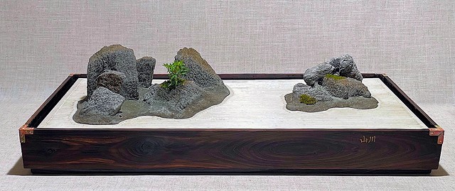 A tabletop version of a traditional Japanese garden, with two rock groupings, live plant, mosses, and a "raked gravel" surface