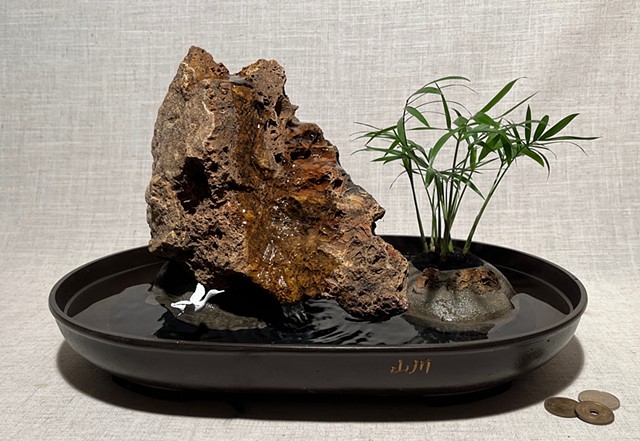 miniature pump hidden inside rock sends water cascading down rock face; miniature palm in separate concrete planter