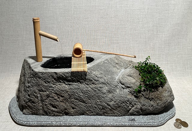 A stone Japanese garden fountain with bamboo ladle and live ivy plant