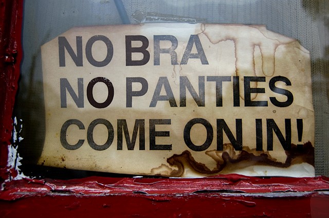 Old tattered sign in window of a Chicago bar that says No Bra No panties, Come on in photographed by Lucy Mueller