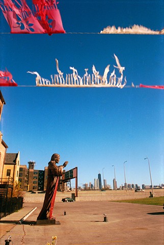 Giant Jesus Statue in a parking lot by Illinois 90/94 in chicago with papel picado or Mexican paper flags in the foreground photographed by Lucy Mueller 
