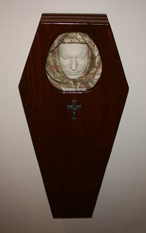 Mixed Media Sculpture assemblage featuring  reclaimed Victorian moldings (coffin sides), ¾” cabinet grade plywood (base and lid), foam, cloth, acrylic paint, wood stain, wood patch, glass and metal crucifix.
